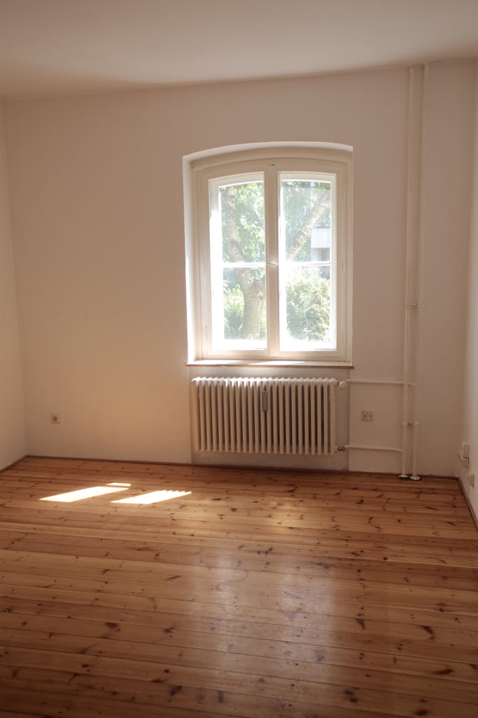 Spacious empty room with wooden floor and large window in Berlin, ideal for interior planning.